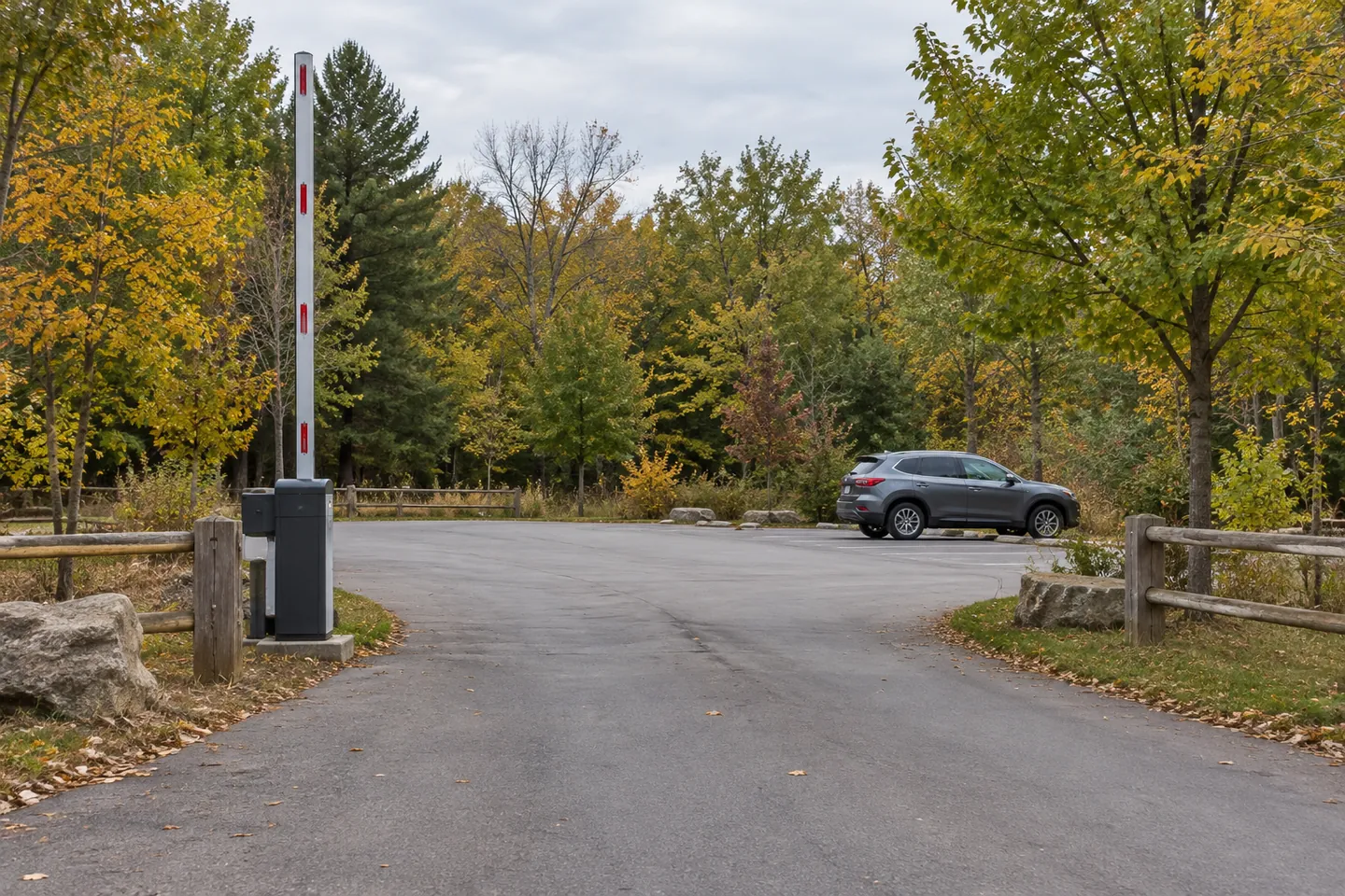 A paved park vehicle entrance with a raised barrier and a car parked beyond